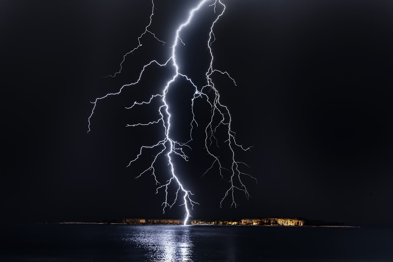 Dramatic lightning bolt over the ocean at night, illuminating the coastal landscape.